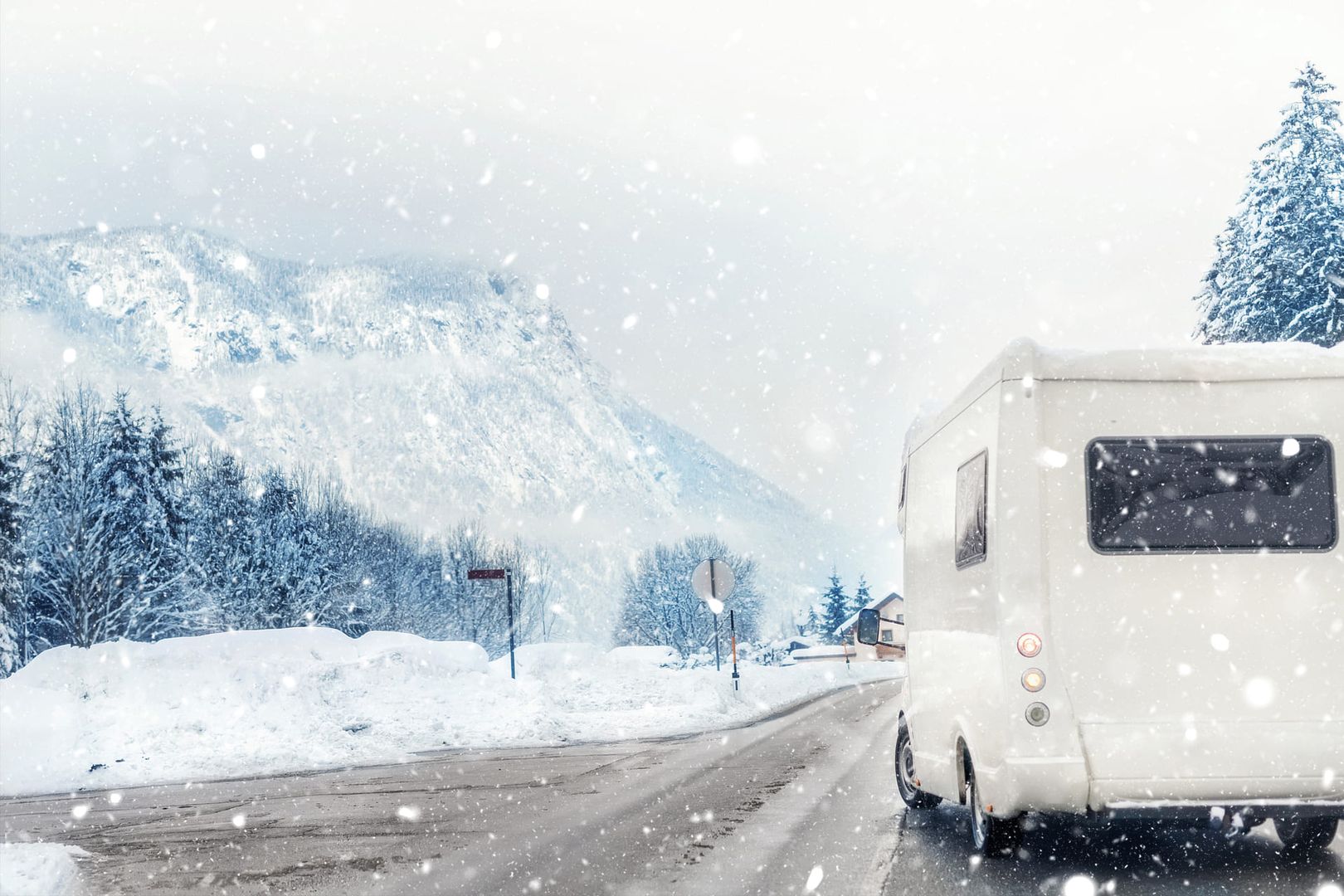 Wohnmobil von hinten bei Schneefall vor verschneiten Bergen